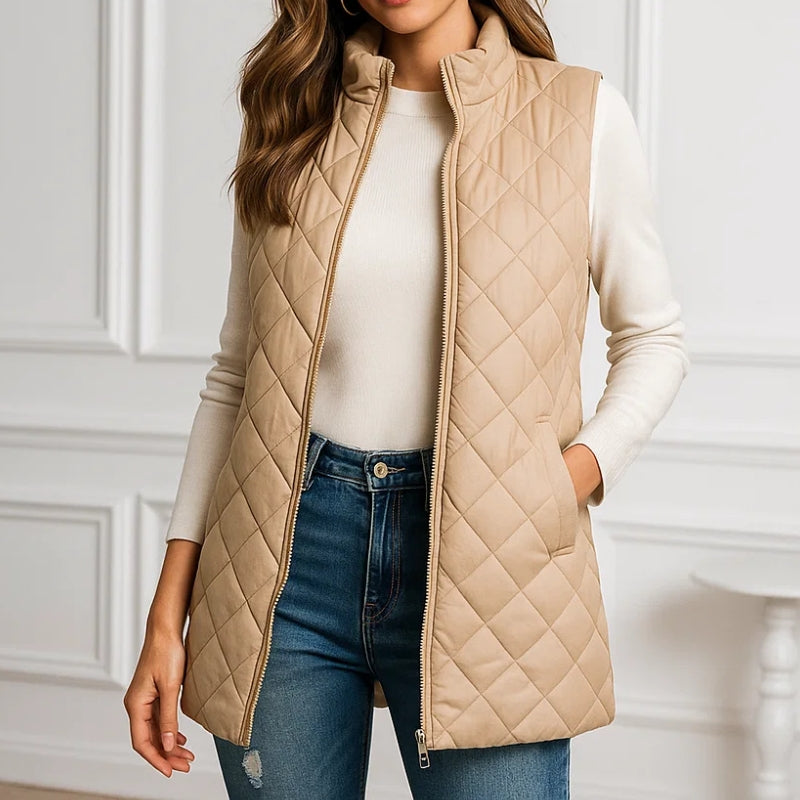 Person wearing a beige quilted vest over a white shirt and blue jeans against a white wall.