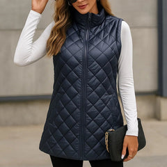 Woman wearing a navy quilted vest over a white long-sleeve shirt, black hat, and sunglasses.